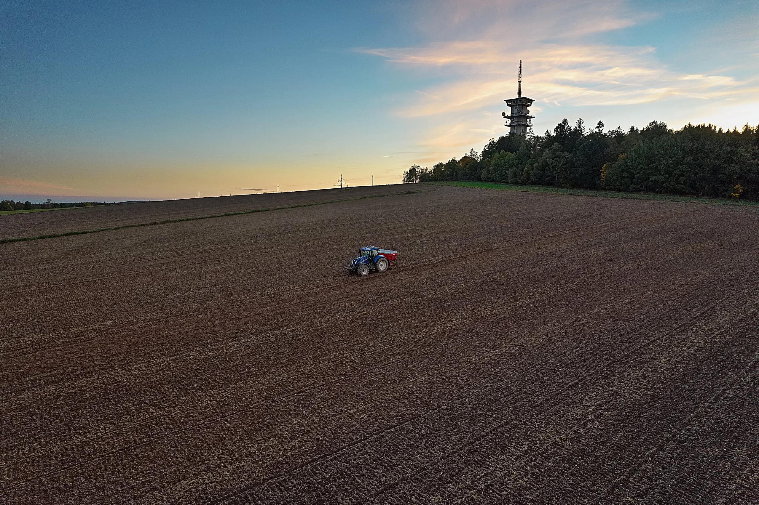 Traktor na zoraném poli, na obzoru rozhledna na Zelené hoře