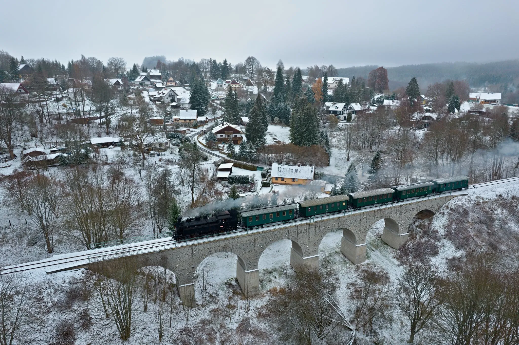 Mikulášský parní vlak přejíždí kamenný viadukt u zasněžené vesnice