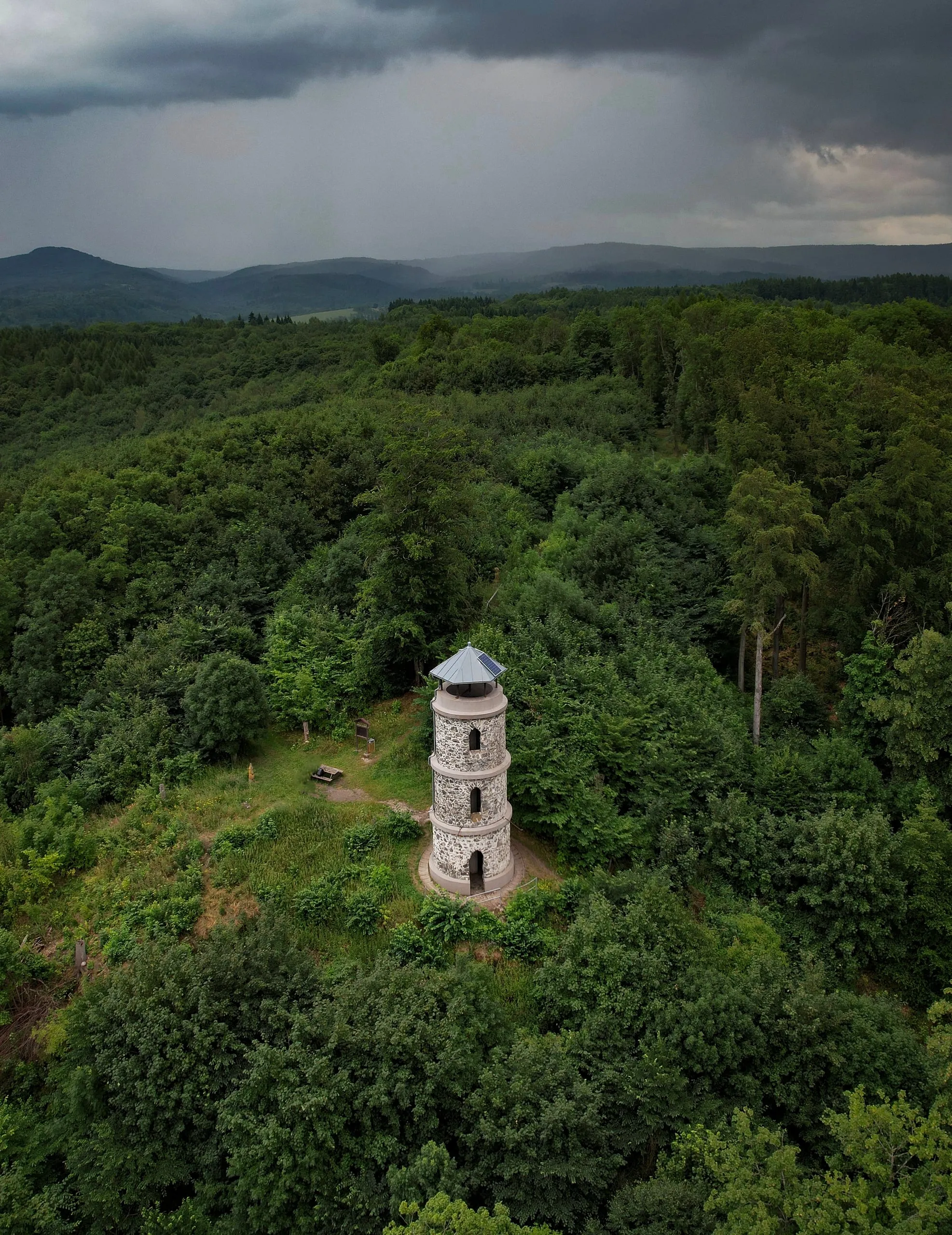 Kamenná rozhledna Bučina na mýtině, nad kopci se blíží bouřka