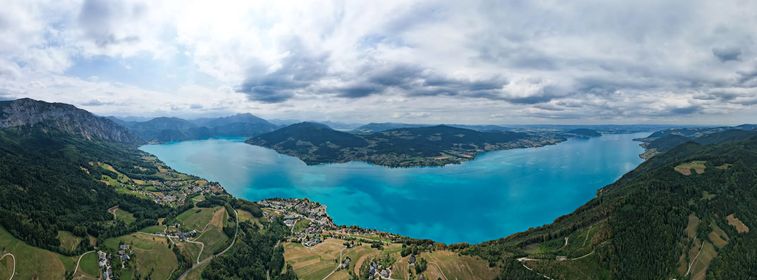 Panorama tyrkysového jezera Attersee mezi zalesněnými svahy