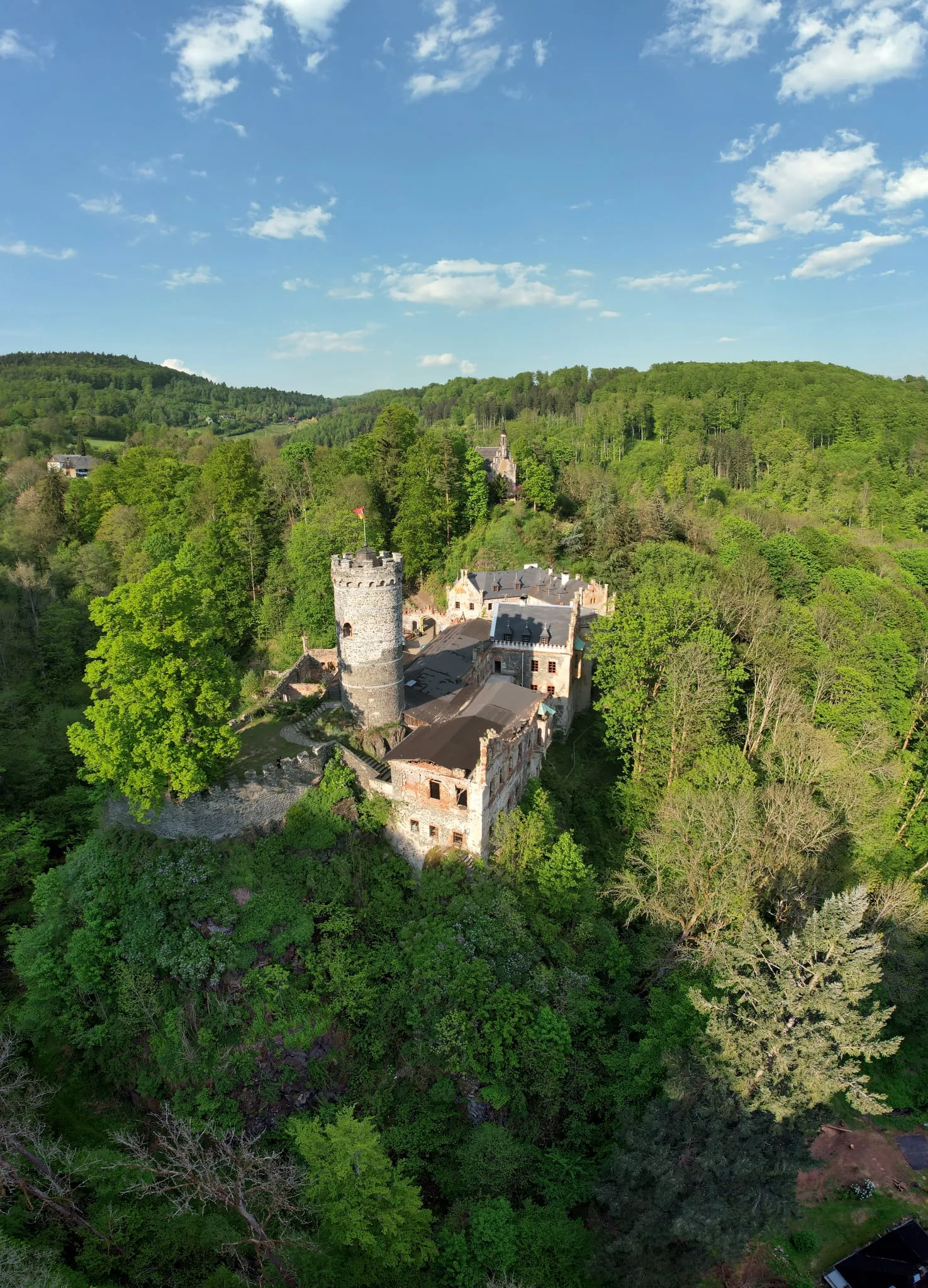 Horní hrad s kulatou věží uprostřed jarního lesa v Krušných horách