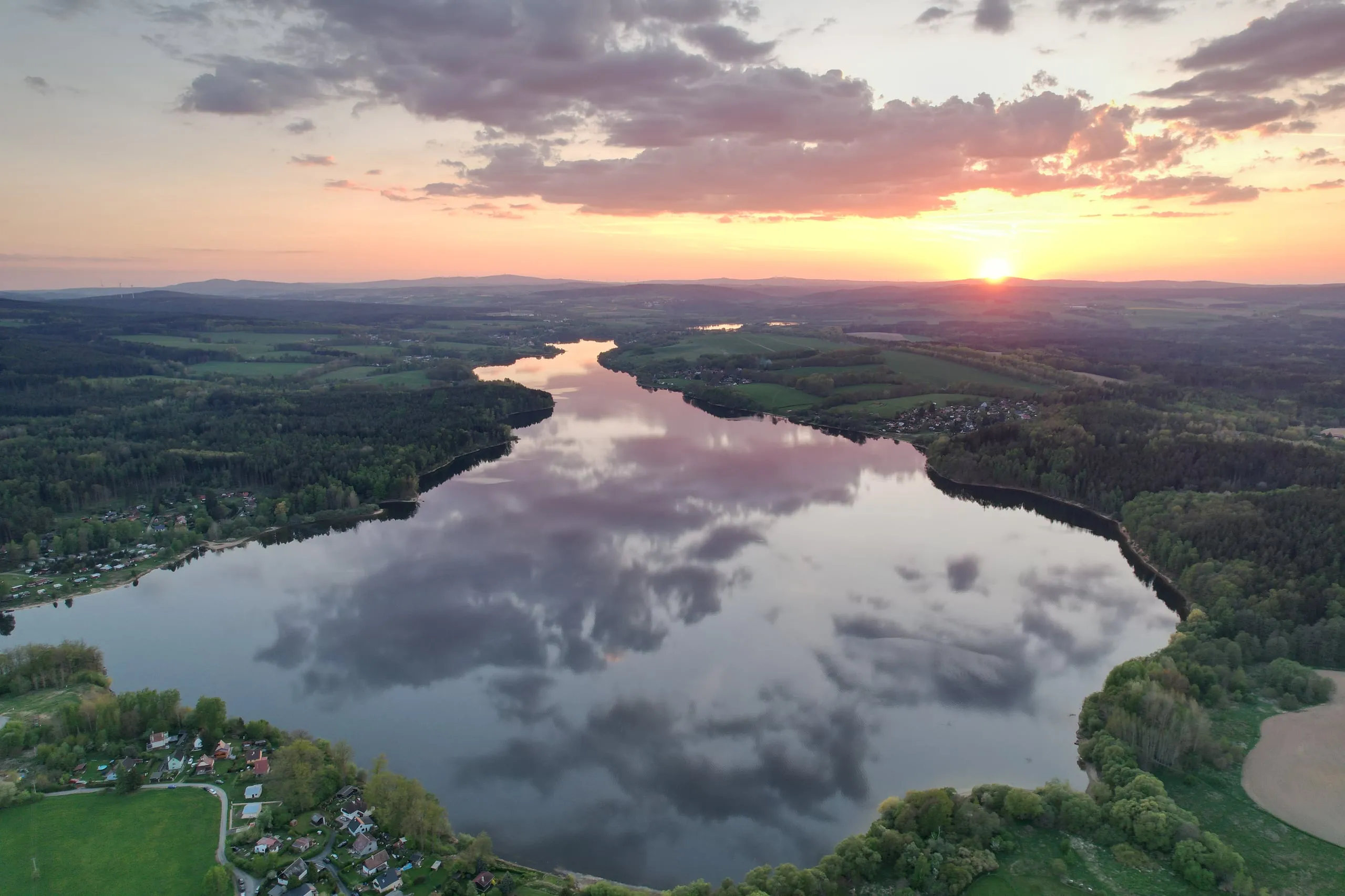 Vodní nádrž Skalka při západu slunce, na hladině se zrcadlí oblaka