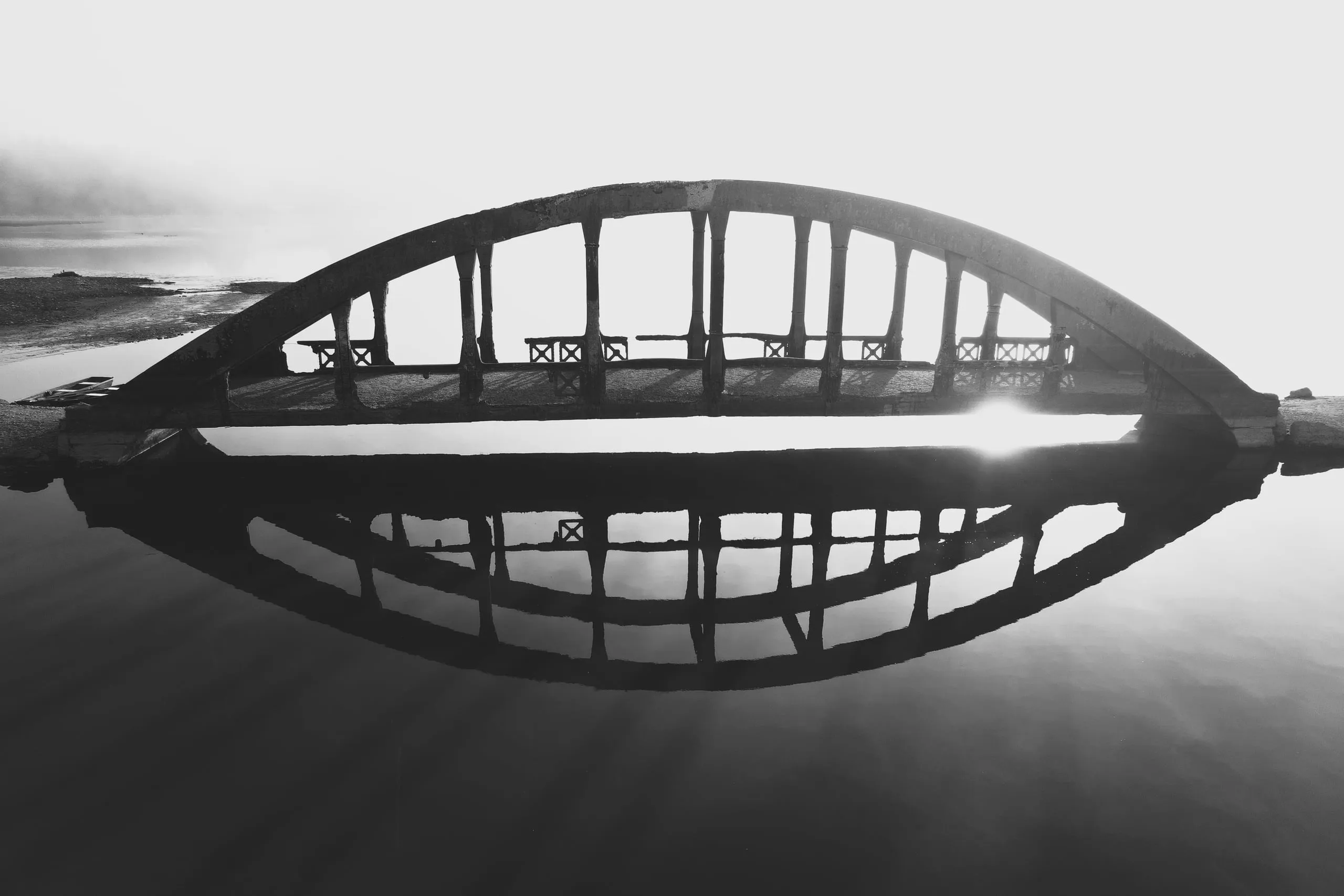 Černobílý snímek zatopeného obloukového mostu u Všeboře a jeho odrazu ve vodě
