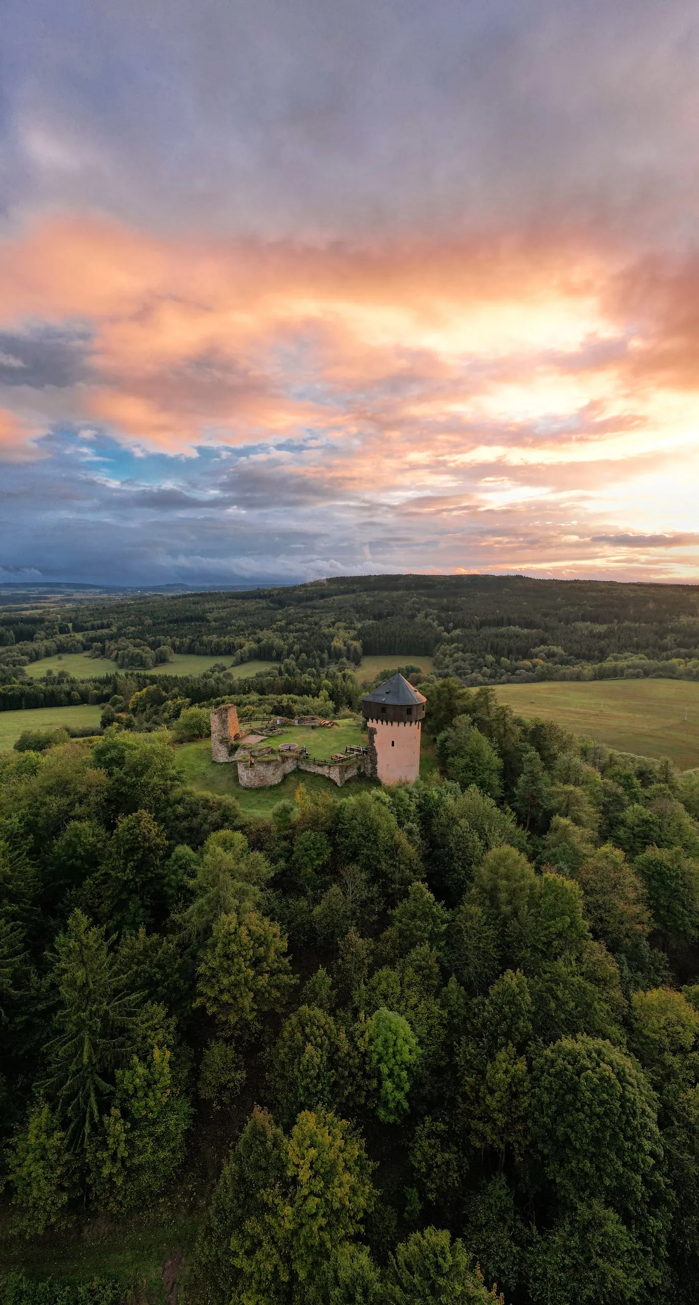Zřícenina hradu s věží nad lesem, obloha po západu slunce